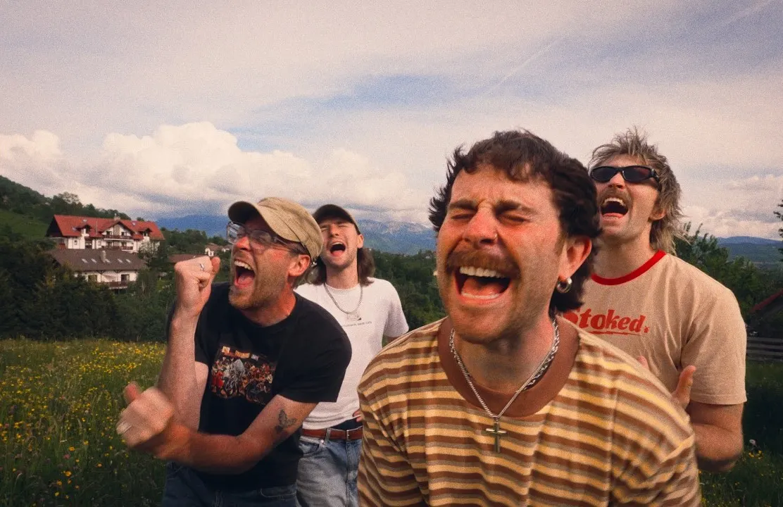 Sam Tompkins and three friends shouting and laughing in a wildflower meadow, mountains behind